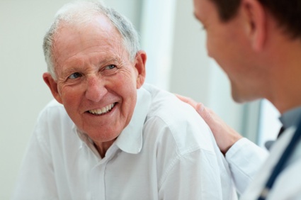 Elderly man in white shirt smiling during conversation with healthcare provider in clinical setting.