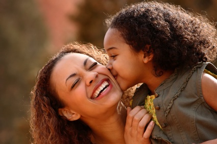 Woman and child smiling joyfully together outdoors in warm, blurred natural setting.