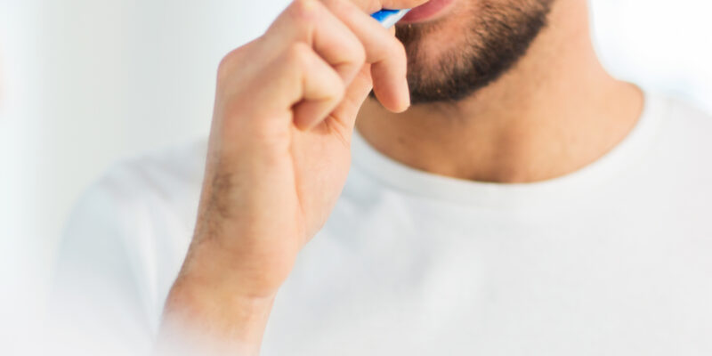 Man brushing teeth with blue toothbrush against white background.