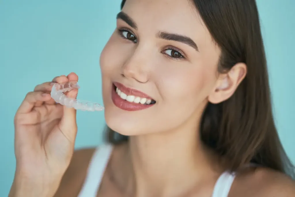 Woman holding clear aligner tray and smiling, demonstrating SureSmile teeth straightening treatment.